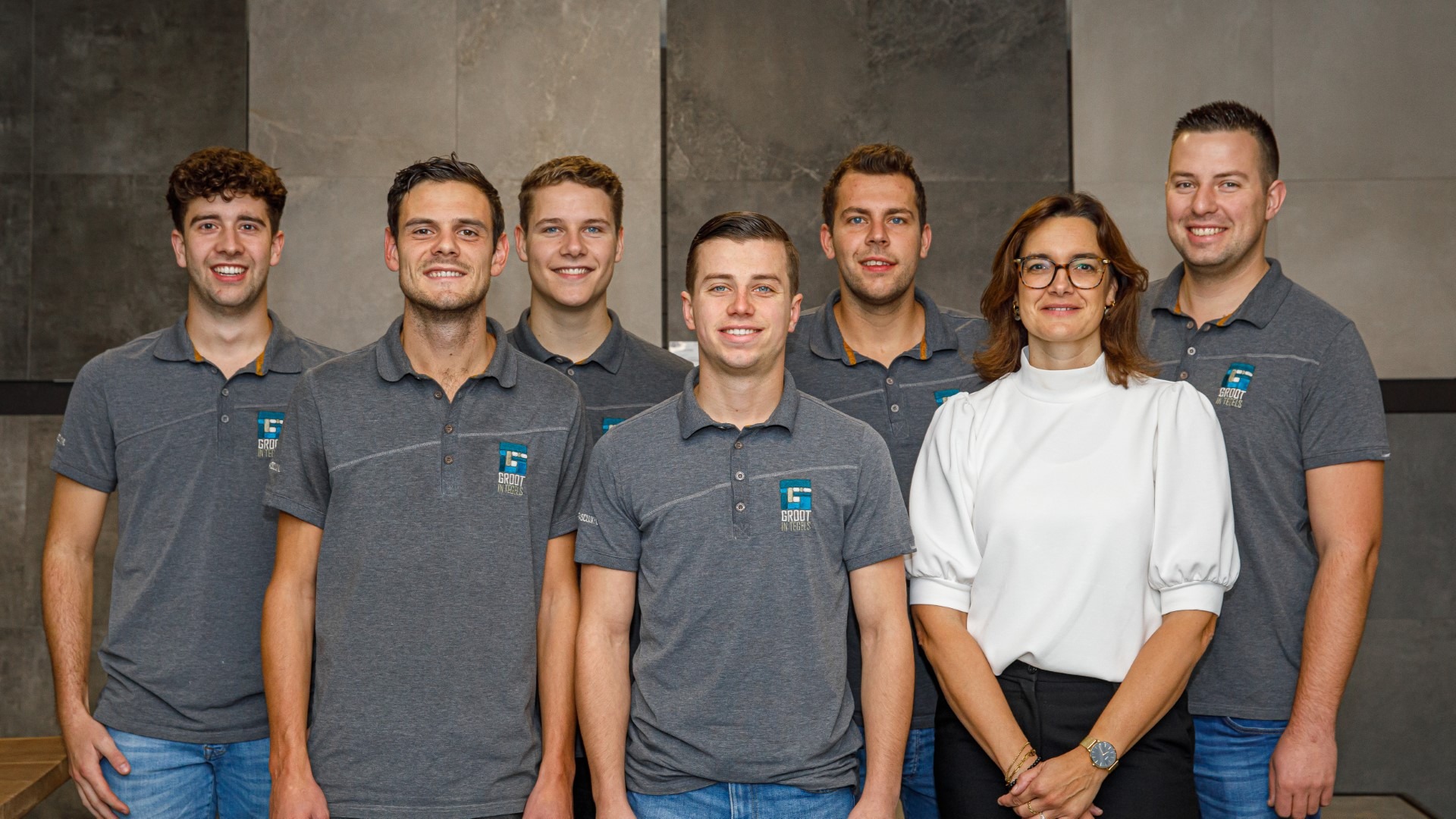 Een sfeervolle groepsfoto van het voltallige personeel van tegelbedrijf Groot in tegels, waarop het vakkundige en enthousiaste team vol trots en met een lach samen poseert.