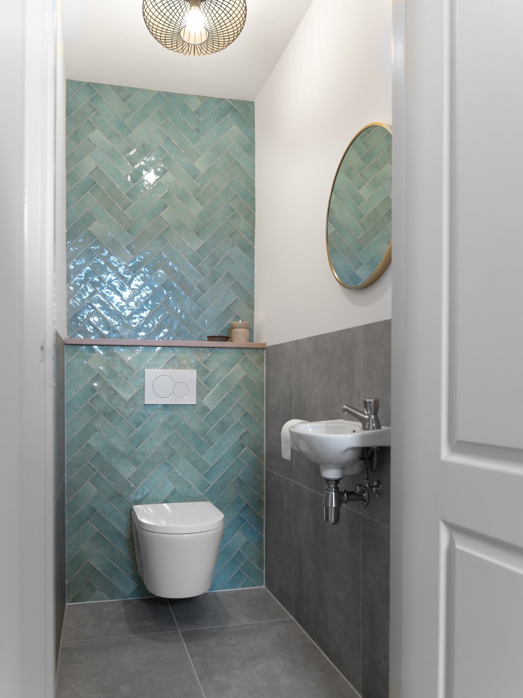 Ronde gouden toiletspiegel in een modern ingerichte toiletruimte, sfeervol gecombineerd met een compact wasbakje en een opvallende tegelwand.